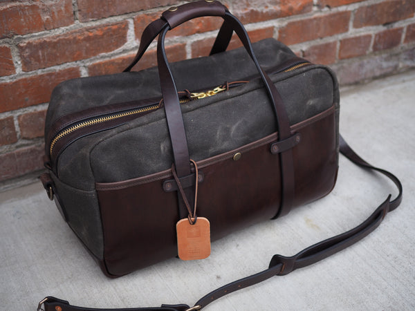 Dark green canvas bag measuring 20 inches long, 10 inches wide and 12 inches tall. Dark brown leather bottom and front pocket. Two dark brown leather straps riveted to front pocket with copper rivets that becomes the handle. Dark brown leather handle wrap. YKK Brass zipper. Dark brown leather shoulder strap with copper rivets and antique brass swivel snaps.