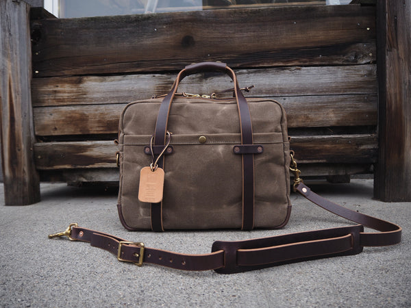 Light brown canvas bag measuring 12 inches tall, 14 inches wide and  6 inches deep.  Dark brown leather bottom.  Dark brown leather handles copper riveted to dark brown leather strip that is sewn near the top of the bag.  Dark brown leather shoulder strap with antique brass roller buckles and swivel snaps.  Copper riveted dark brown leather pocket centered on front of bag.