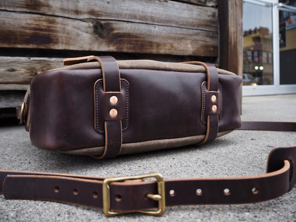 Bottom of bag is dark brown leather with 2 copper rivets attaching each leather handle to bottom of bag.  Dark brown leather shoulder strap with antique brass roller buckles.