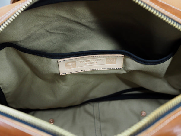 YKK Brass zipper opened of light brown leather briefcase. Inside of bag has laptop pocket on side with Vermilyea Pelle logo.  Bag lined in tan canvas duck fabric.